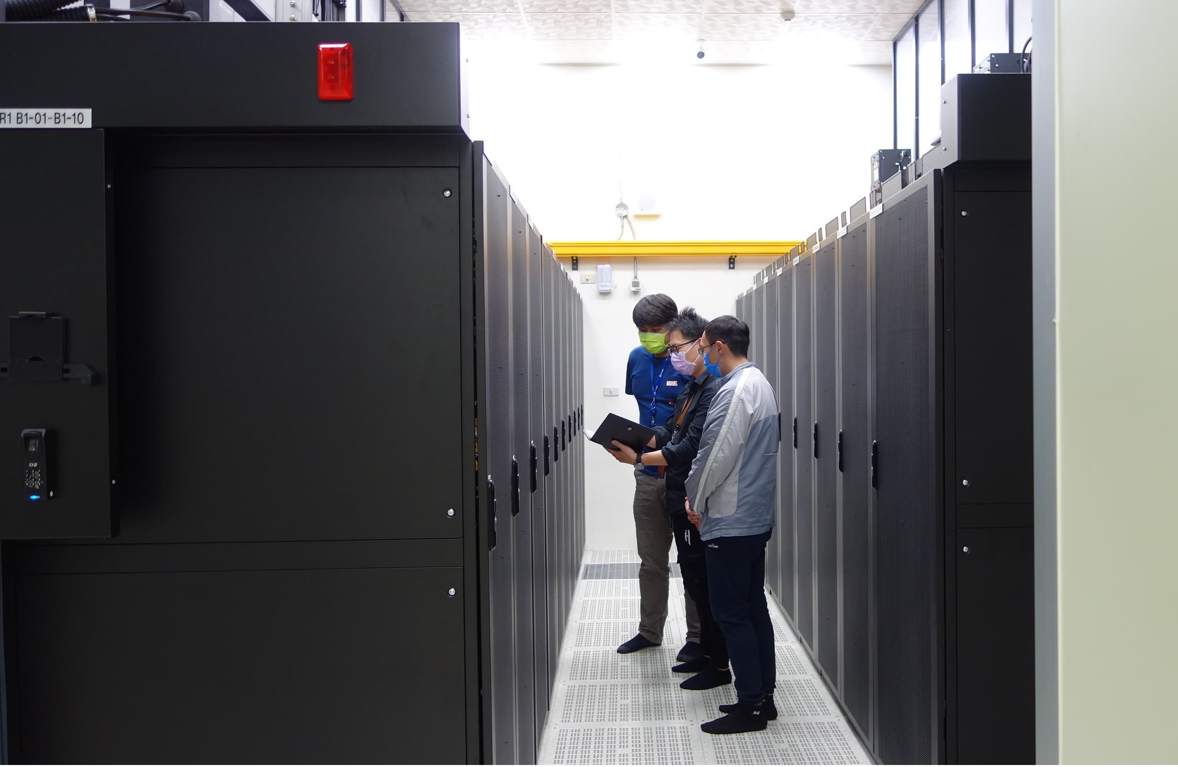 Engineers reviewing equipment in a data-center aisle lined with server cabinets